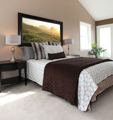 a carpeted room with a high sloping ceiling, two small brigh windows, and a two-person bed wih a bedside table and lamp on each side