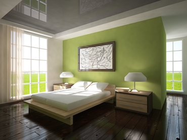room with a hardwood floor, bright windows on two sides, and a two-person  bed with a bedside table and lamp on each side